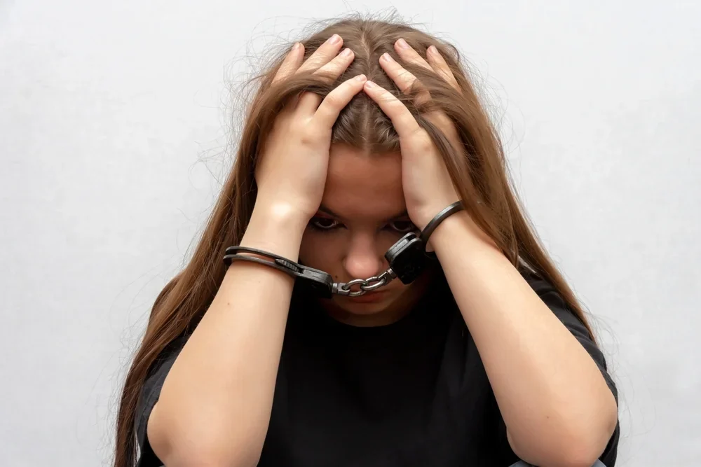 A young girl handcuffed on a gray background