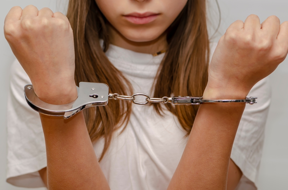 Teenage girl in handcuffs on gray background