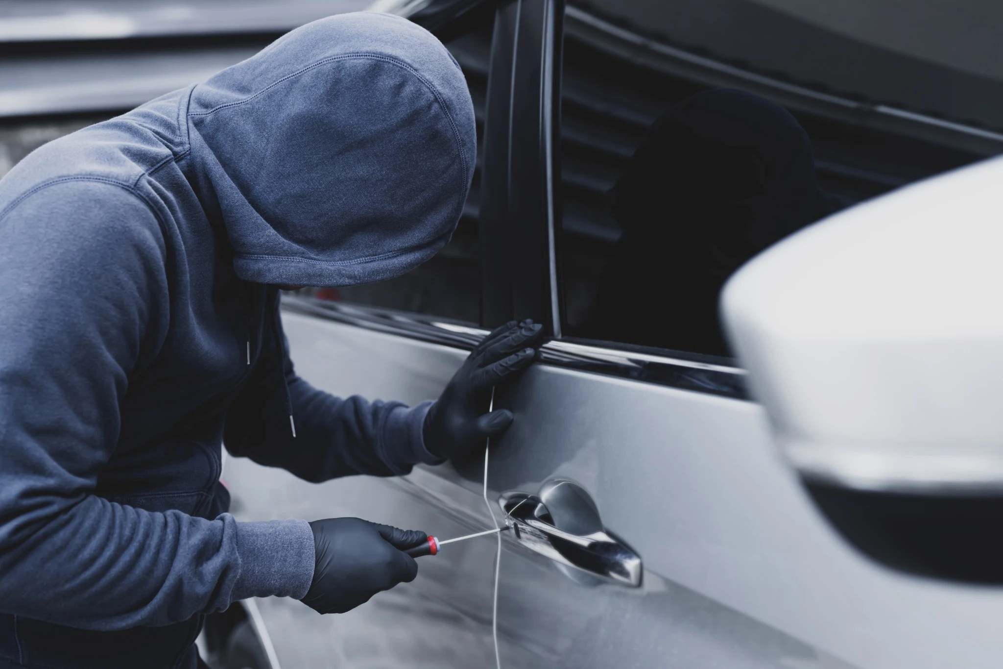 A thief attempting to break into a car by using a screwdriver