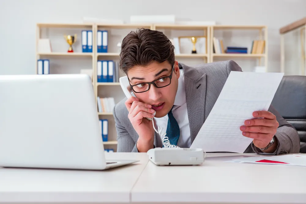 Businessman talking on the phone while reviewing a document at his desk