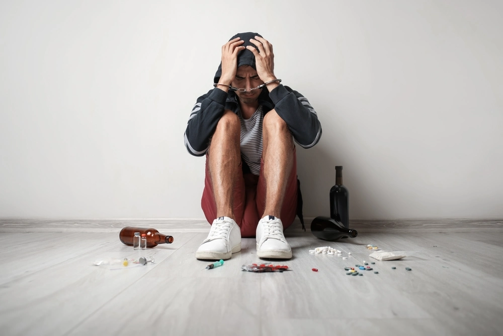 Male junkie with drugs and alcohol sitting on floor