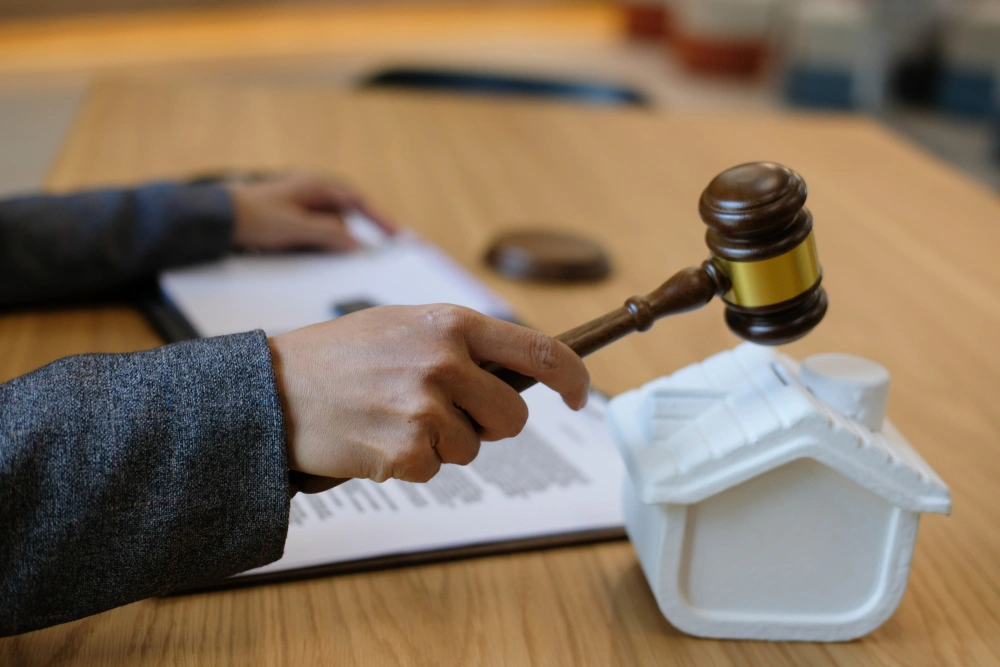 lawyer with judge gavel knocking house model with law document at courtroom