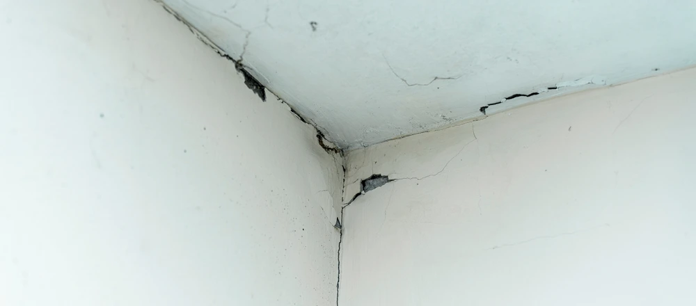 Large cracks are appearing on a white wall and ceiling meeting in a corner.