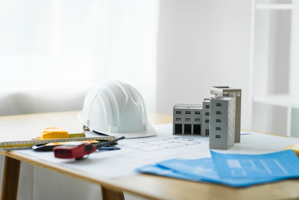Close-up of a table with a blueprint, architect’s tools, and an engineer’s hat