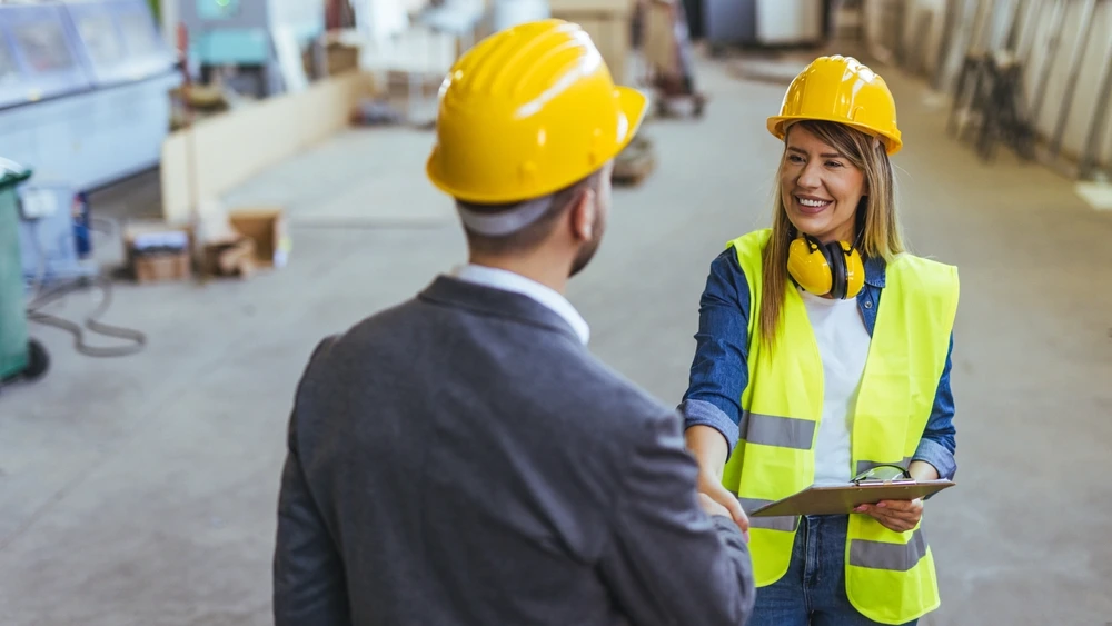 Two individuals in construction gear and safety equipment are shaking hands