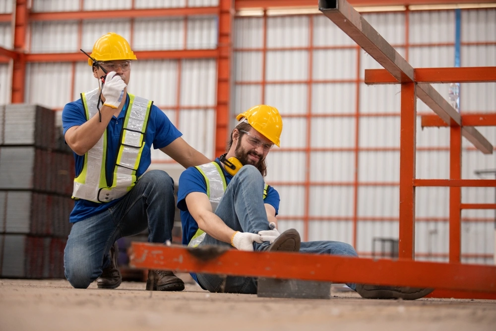 Construction worker injured in workplace accident, holding foot in pain while colleague calls for help