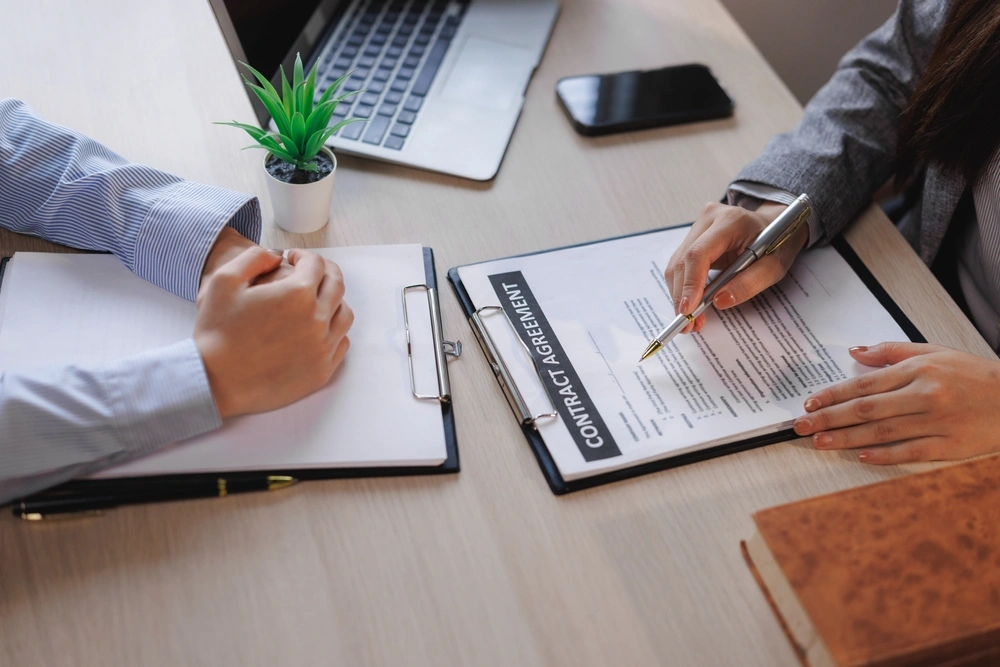 Business partners reviewing contract agreement terms at an office desk.