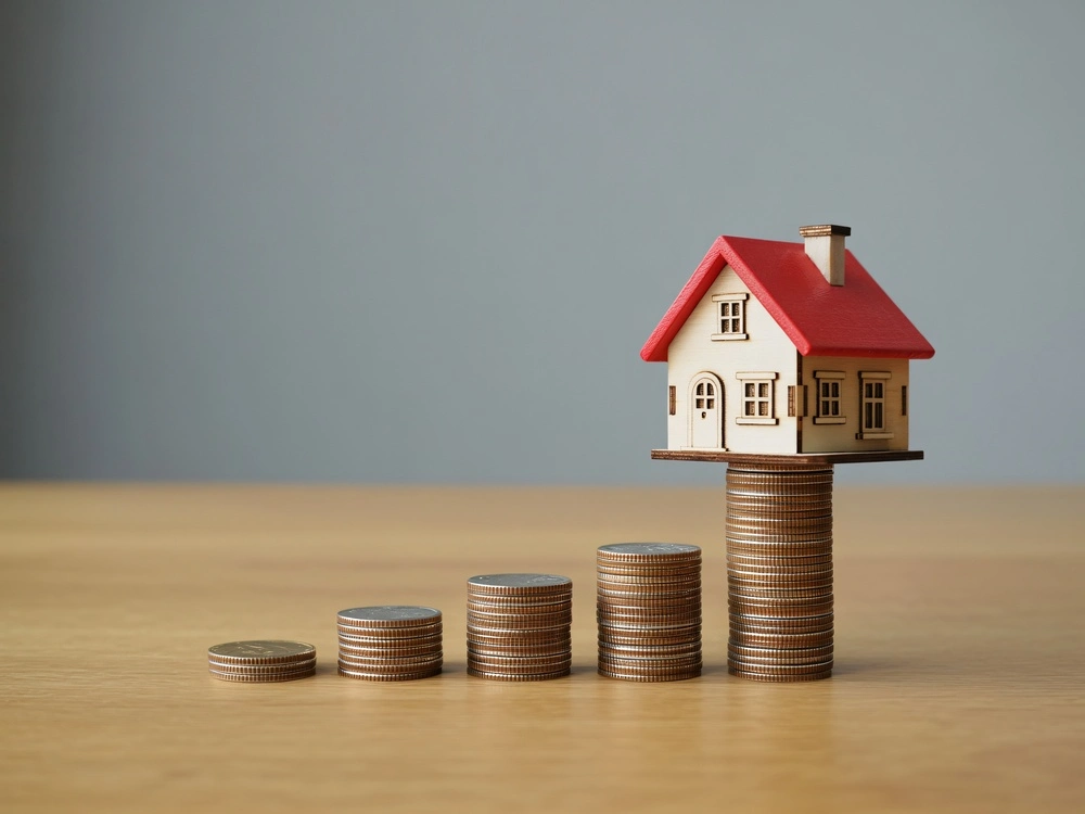 A small house sits atop a stack of coins representing financial growth